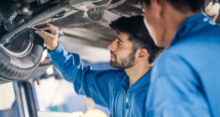 Vehicle service maintenance handsome mens checking under car condition in garage. Automotive mechanic pointing flash light on wheel following maintenance checklist document. Car repair service concept